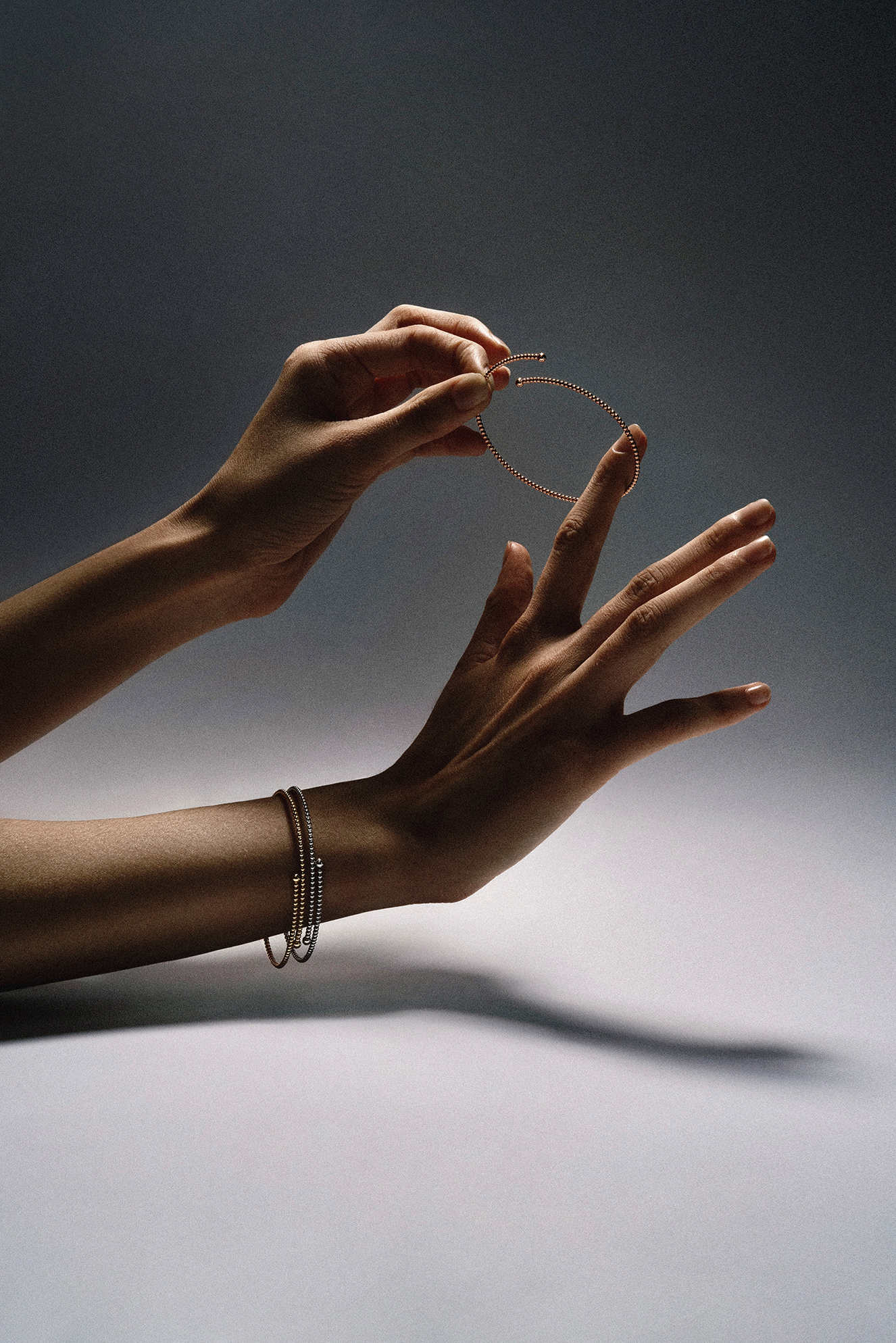 Close-up studio still life of gold jewelry styled with a dark metal tool on a moody gradient background.