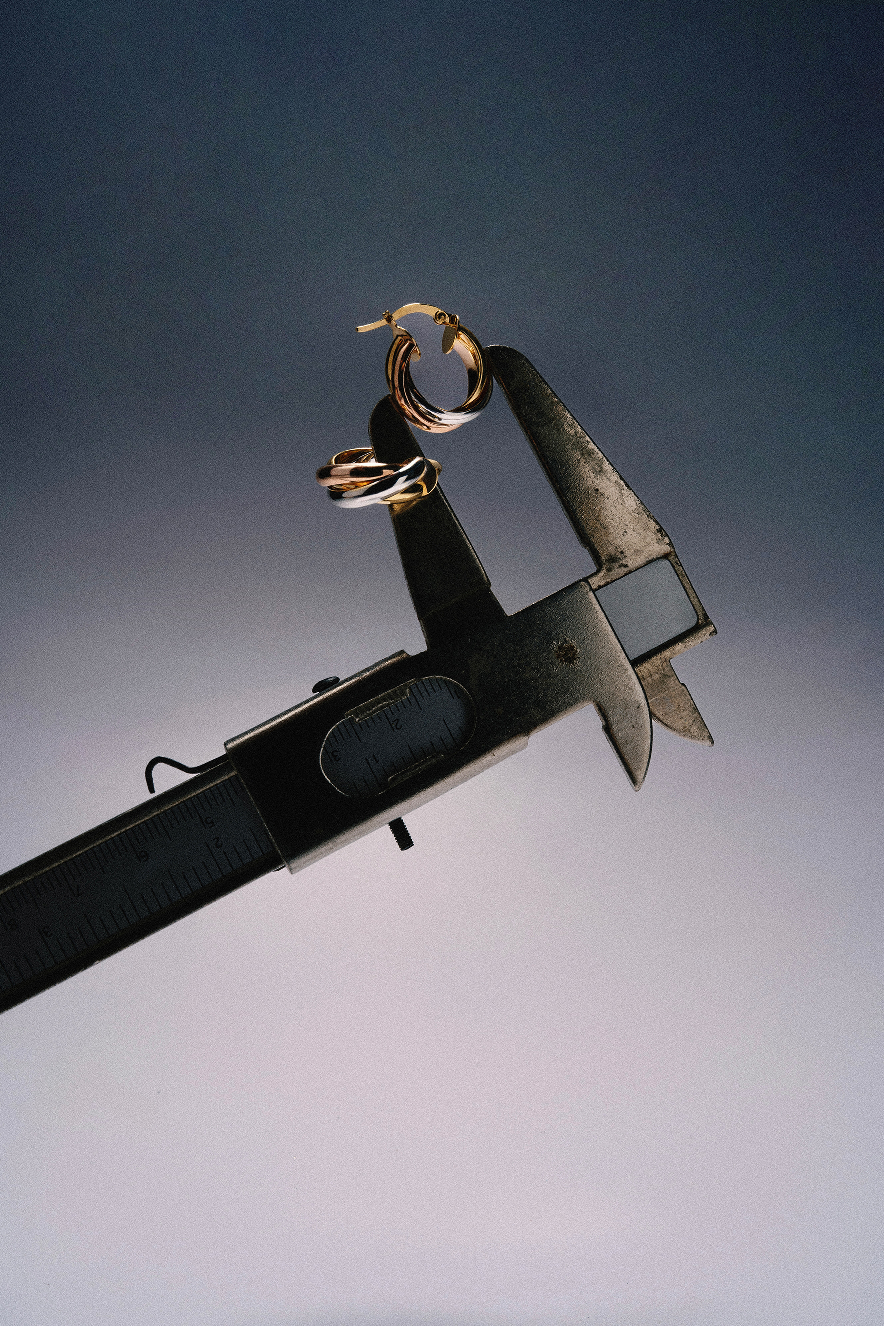 Gold hoop earrings balanced on a caliper in a dramatic studio still life.