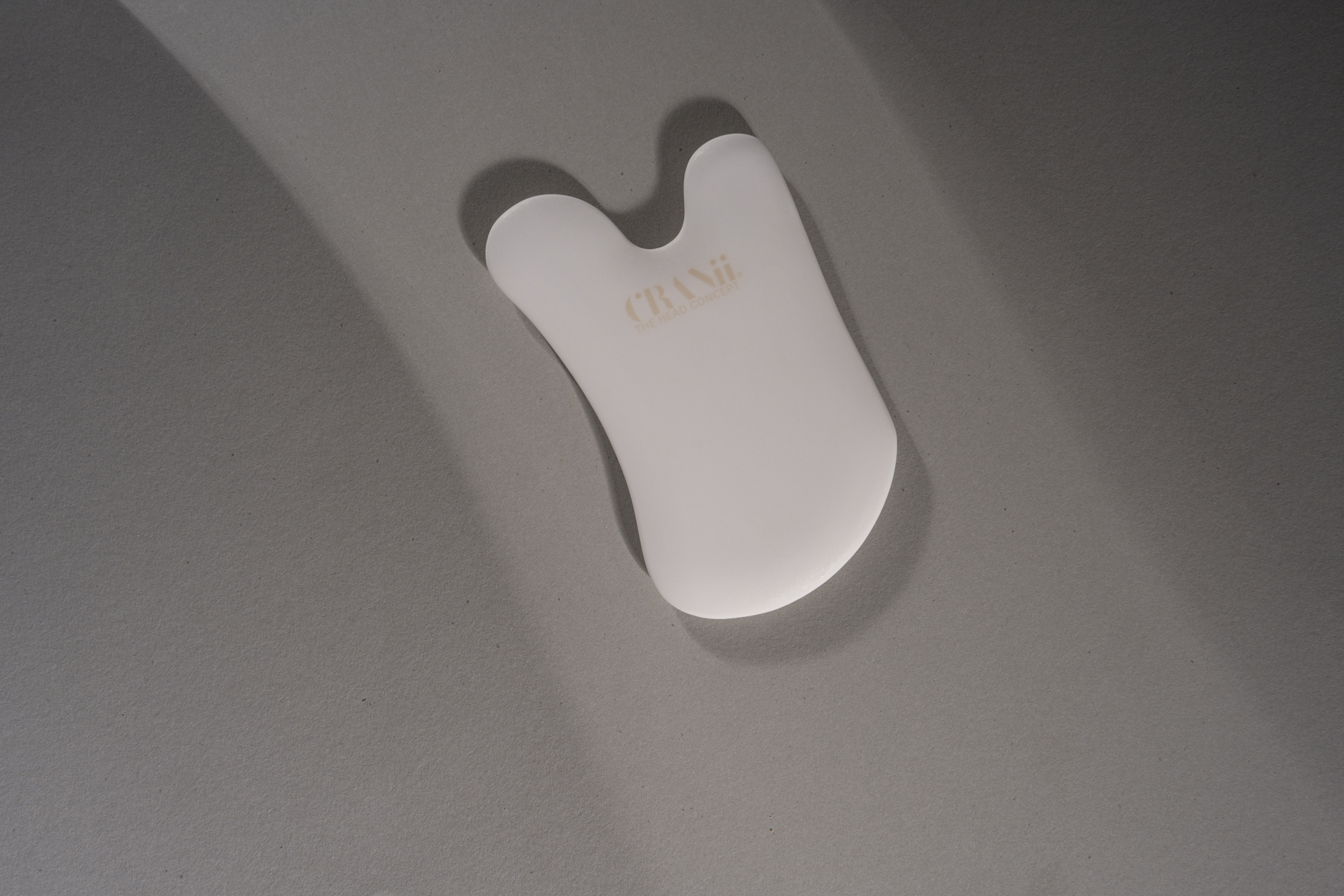 White CRANii ceramic face tool photographed from above on a gray textured surface.