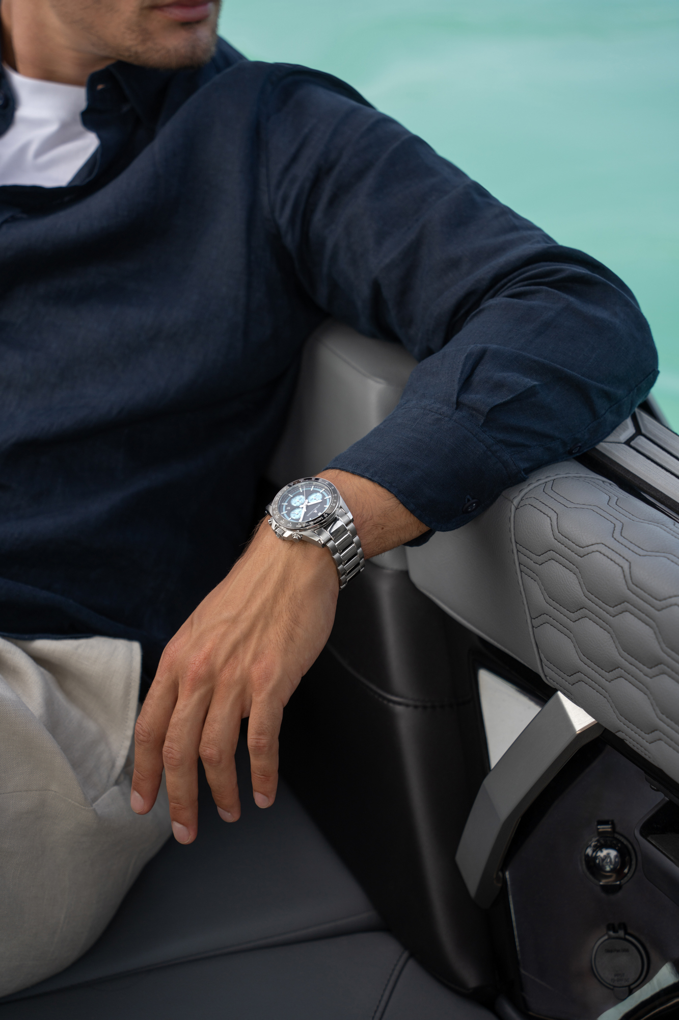Close-up of a man wearing a silver wristwatch while seated in a boat on turquoise water.