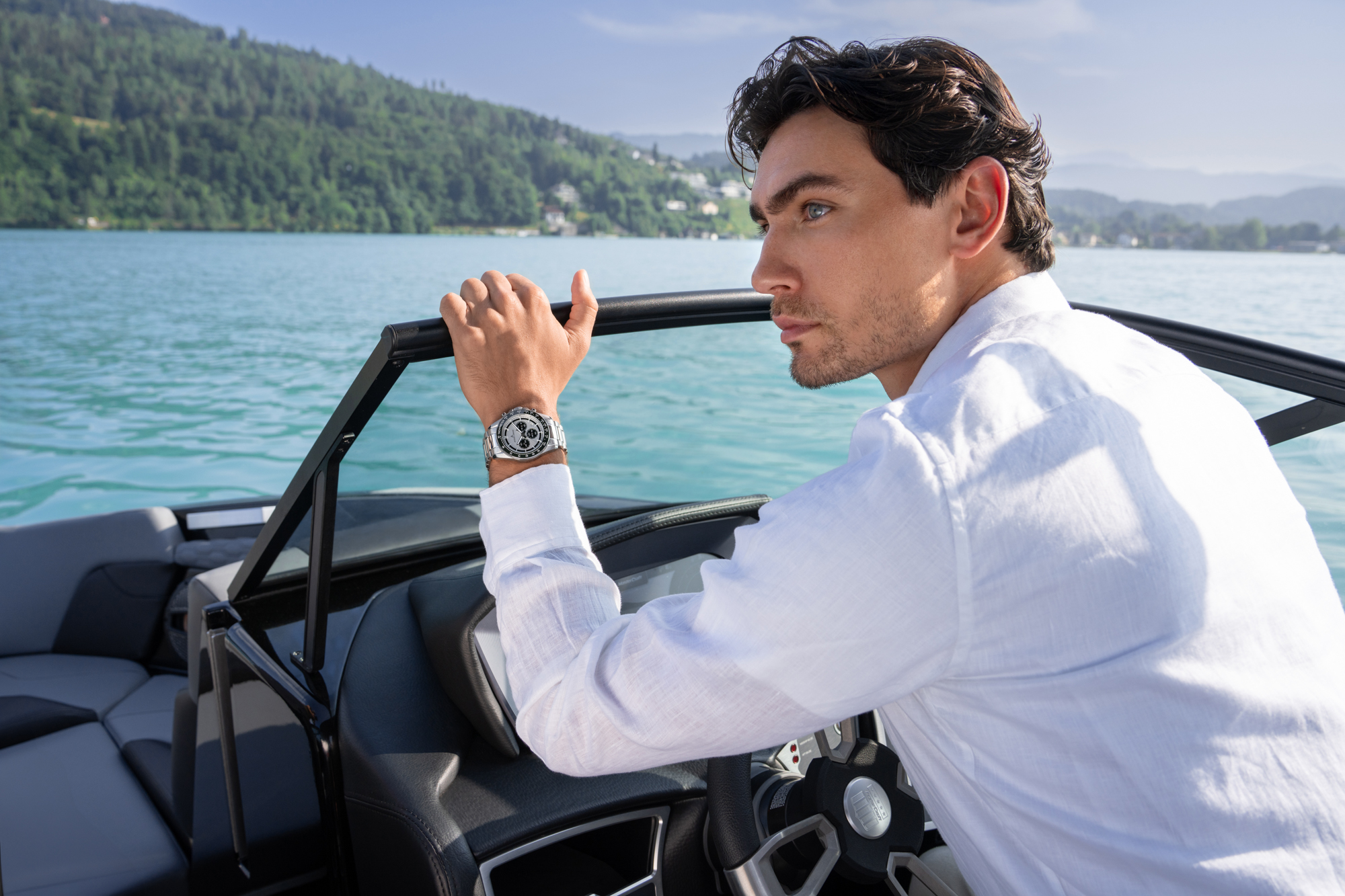 Man in a white shirt steering a boat on a lake, wearing a silver wristwatch.