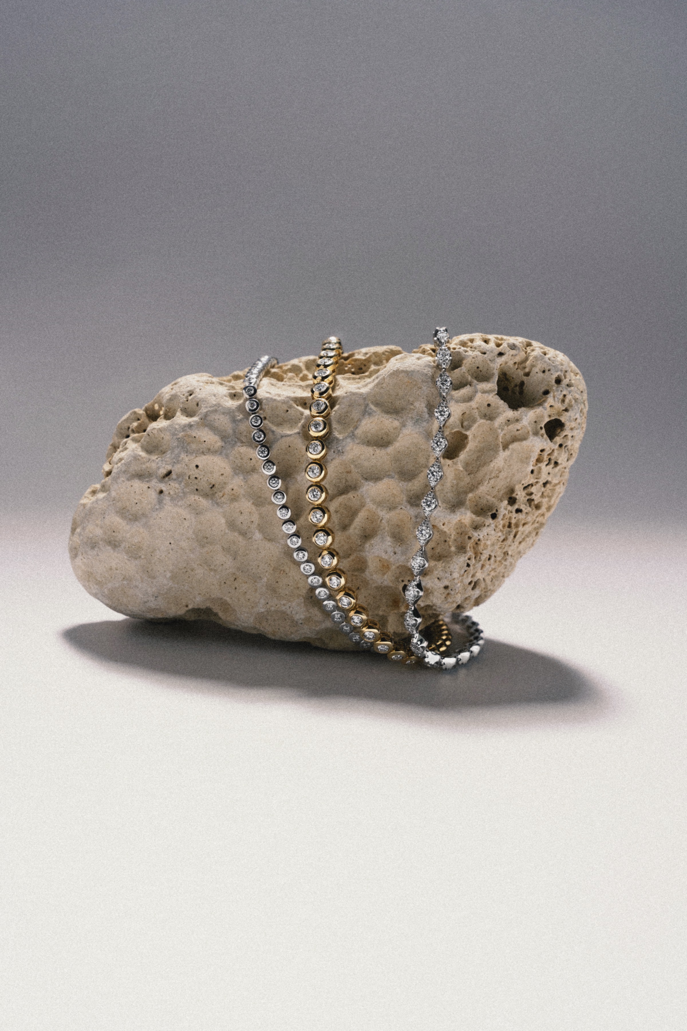 Silver and gold bracelets draped over a textured stone in a studio jewelry still life.