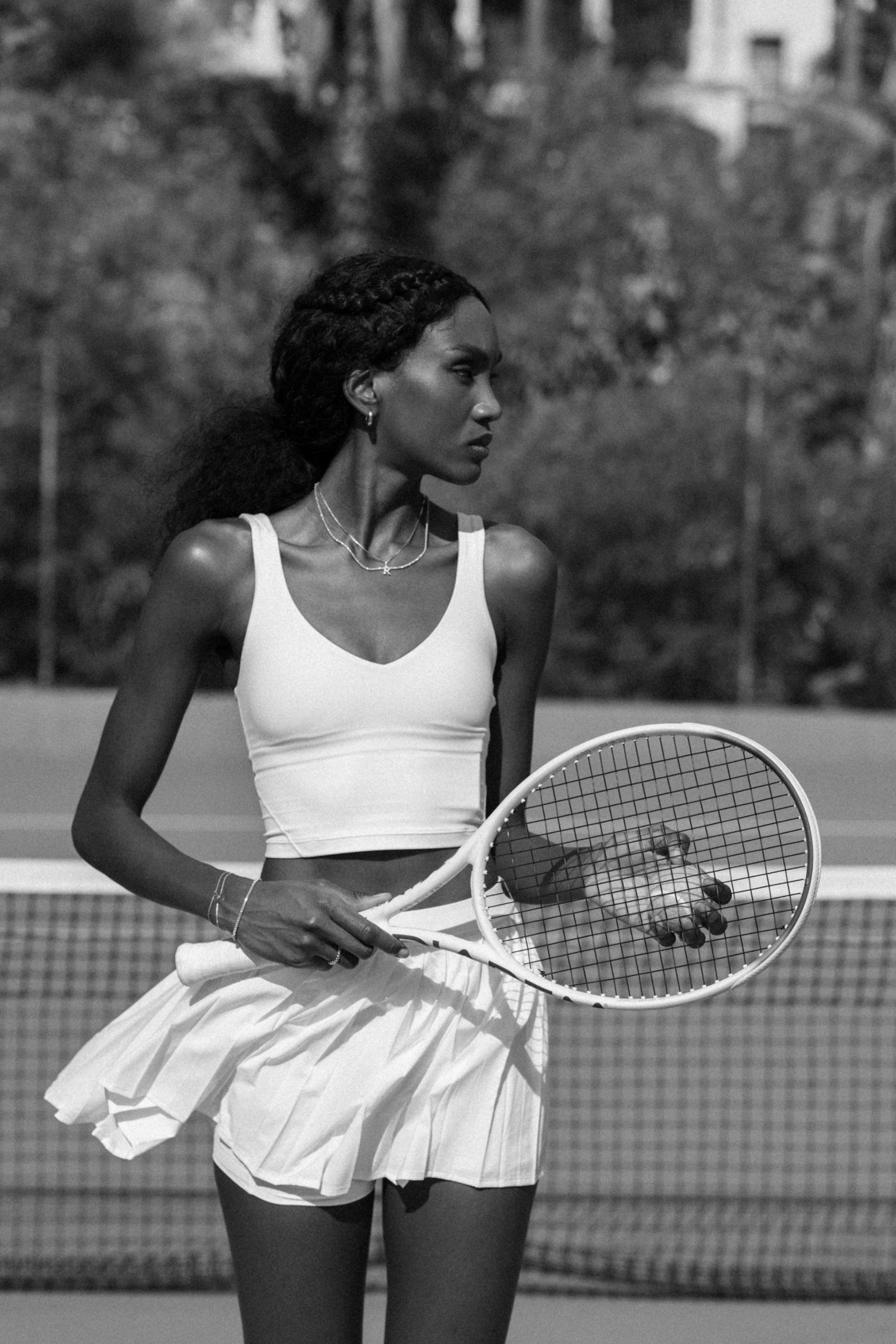 Black-and-white photo of a tennis player in a white outfit holding a racket on the court.
