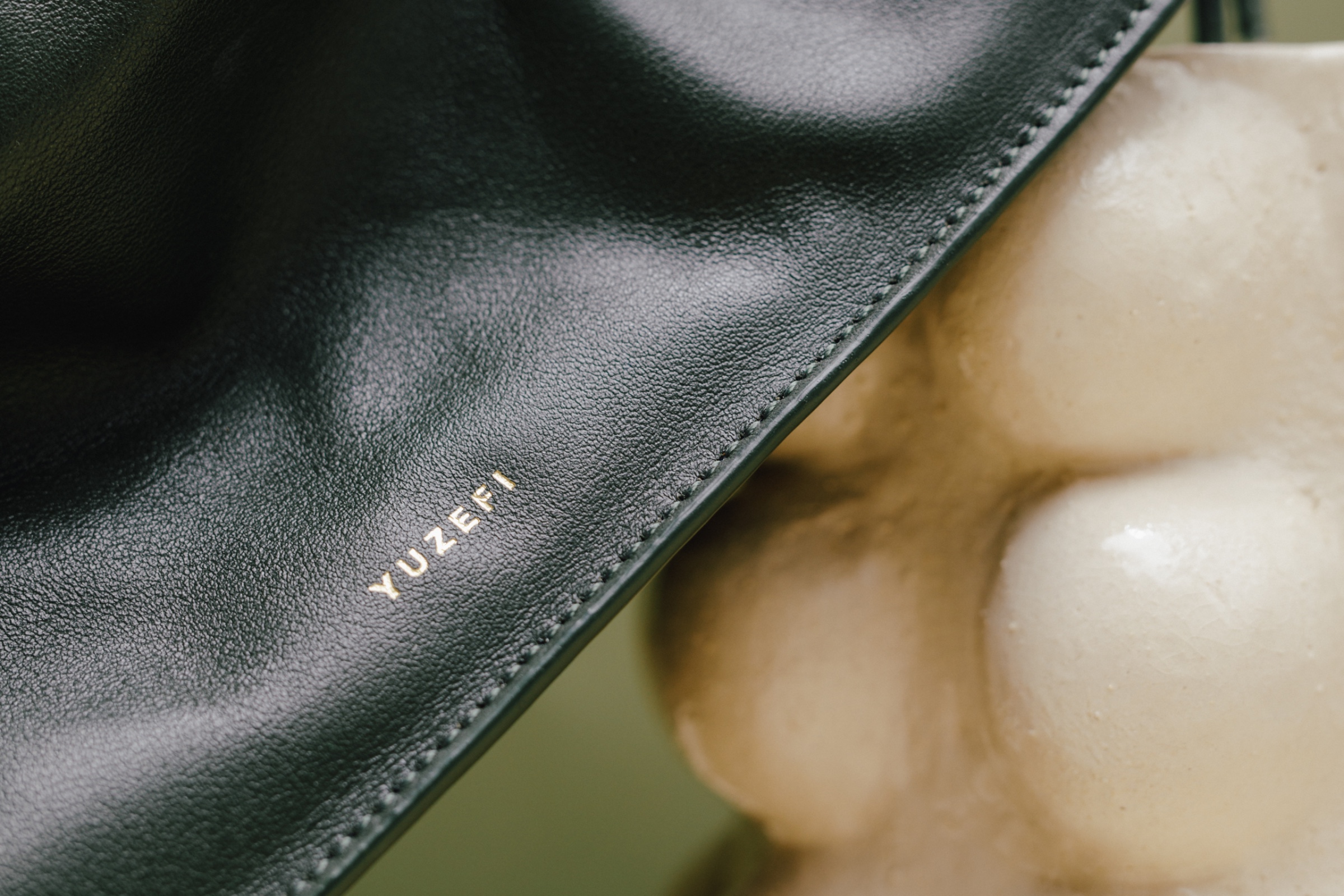 Studio product image featuring an olive green leather handbag in a minimal sculptural setup.