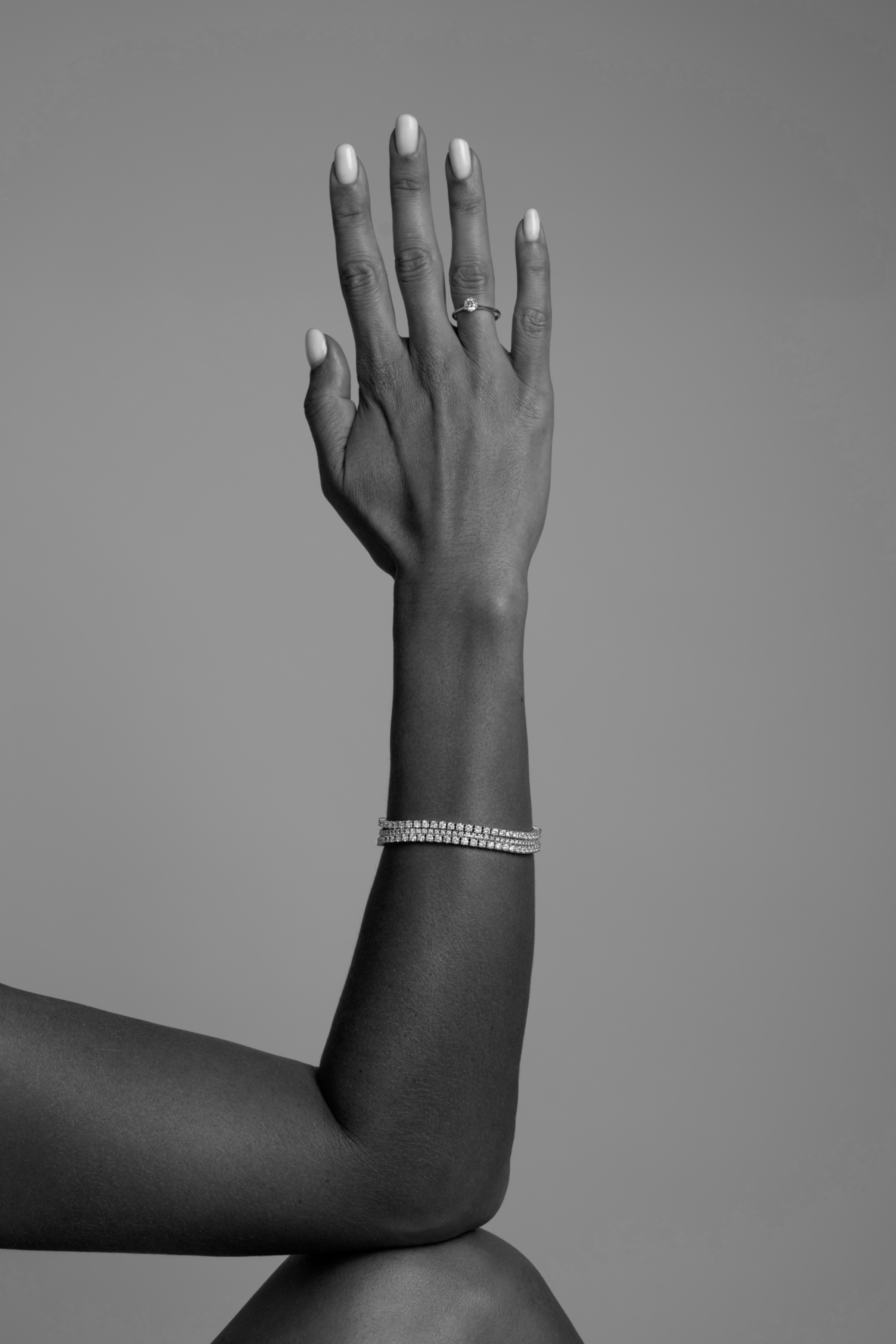 Black-and-white close-up of an arm and hand wearing a bracelet and ring against a plain studio background.
