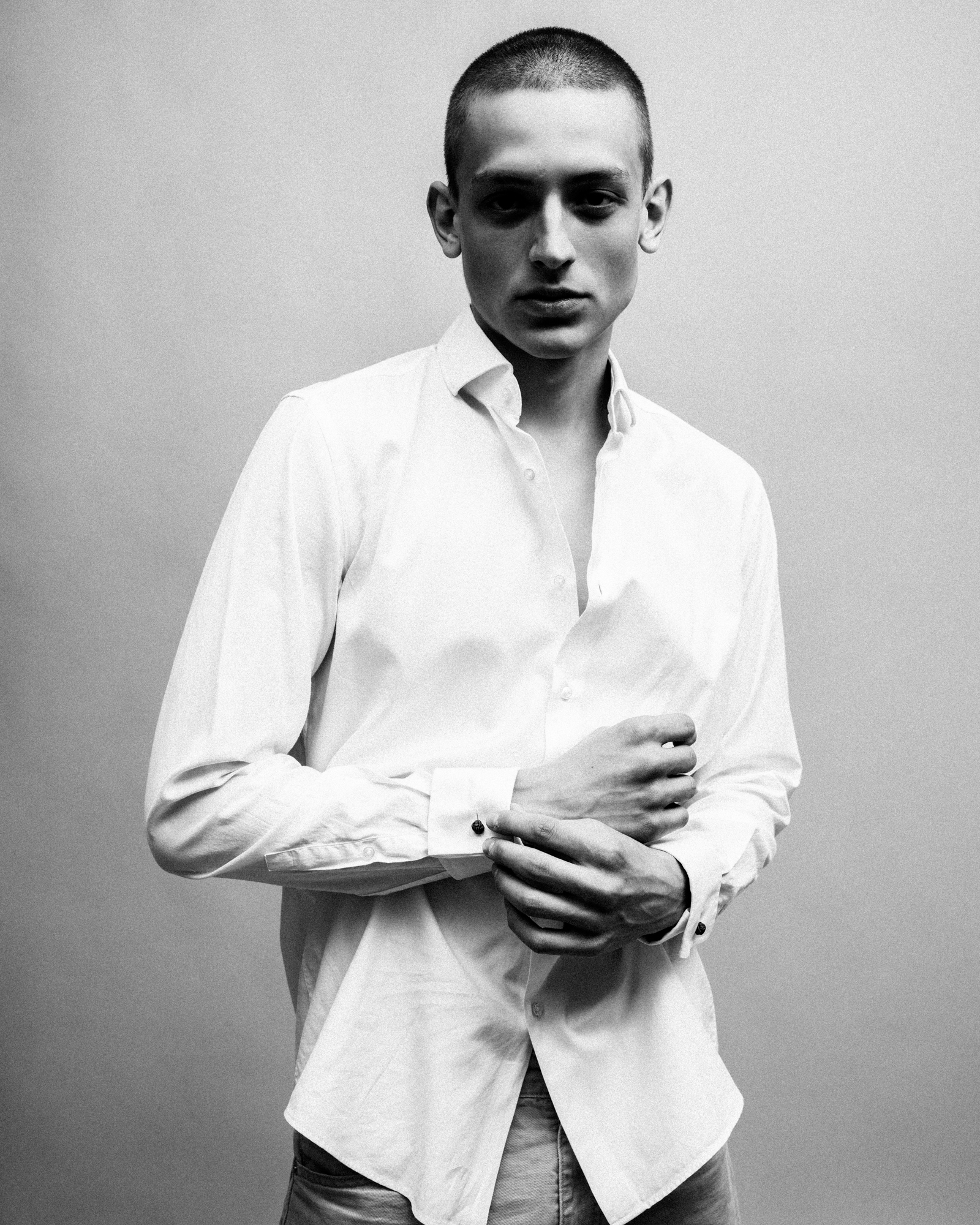 Black-and-white fashion portrait of a man in a white button-down shirt adjusting his cuff.