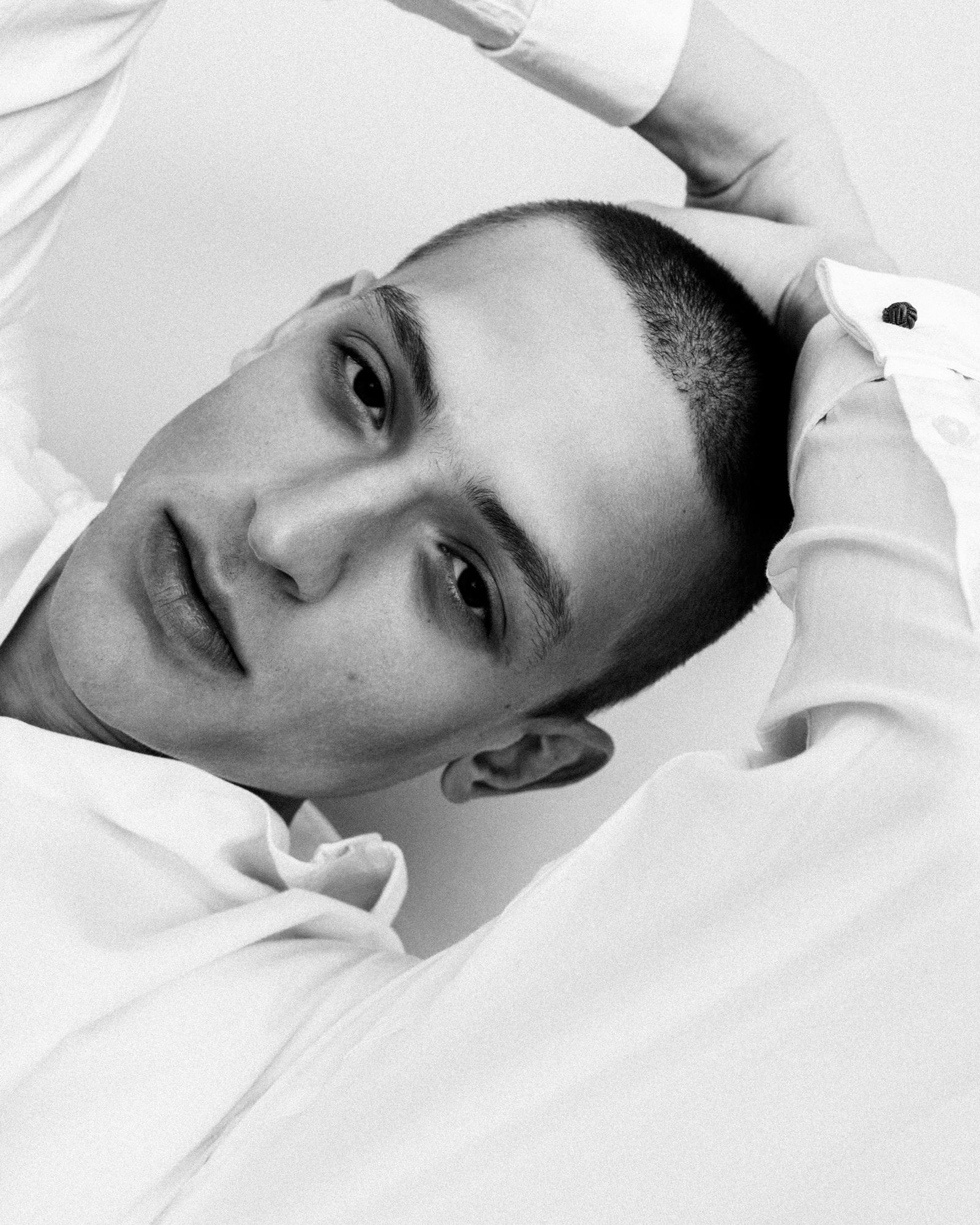 Black-and-white close-up portrait of a man with a buzz cut leaning sideways in a white shirt.