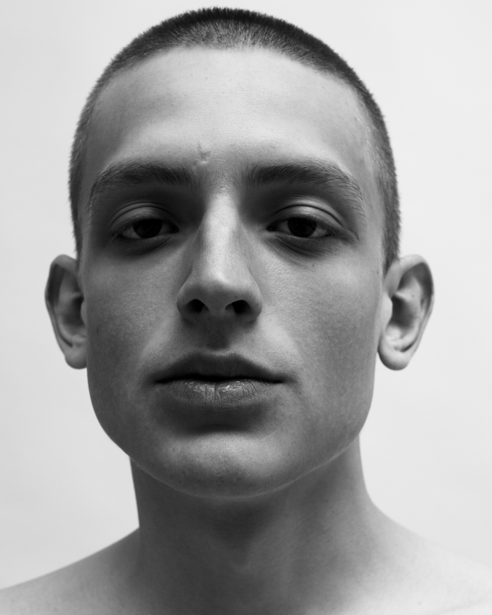 Black-and-white close-up portrait of a man with a buzz cut looking directly at the camera.