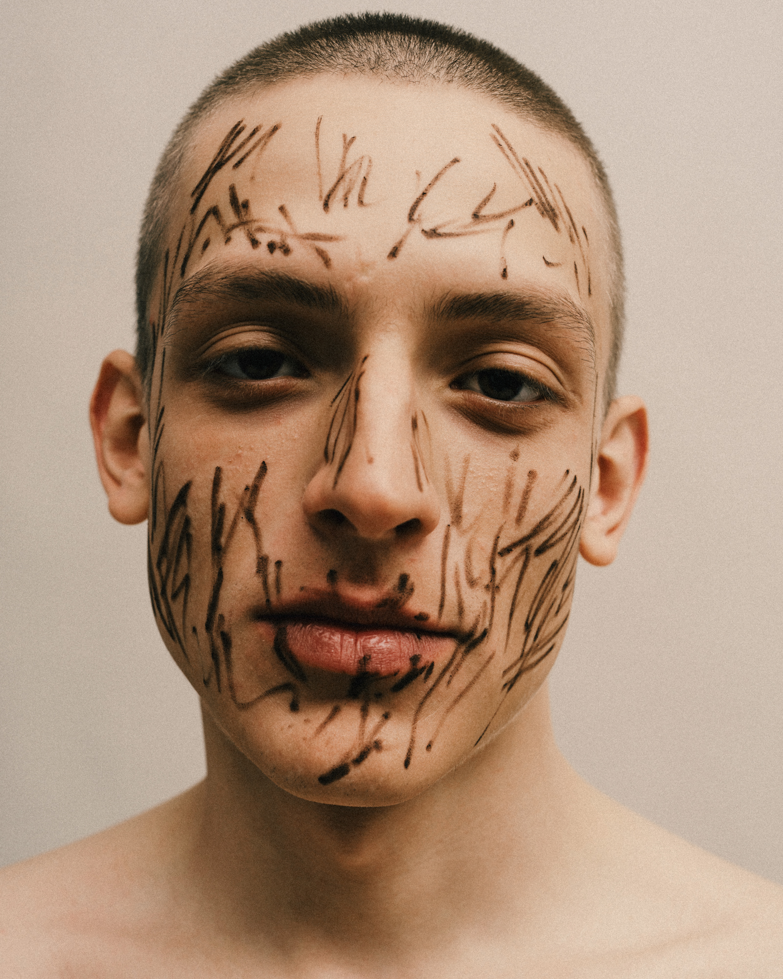 Close-up portrait of a man with dark expressive makeup marks drawn across his face.