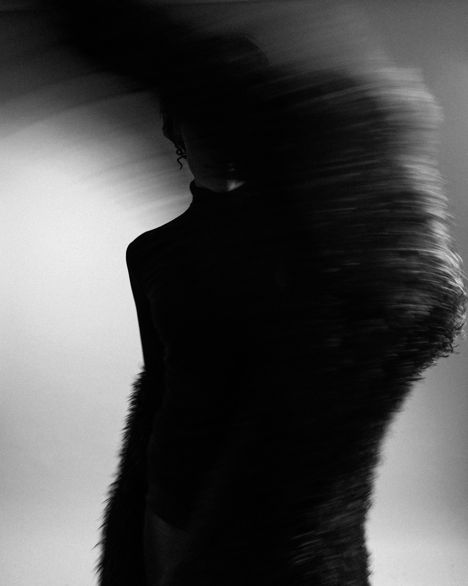 Abstract black-and-white portrait of a model partially hidden behind a sweeping dark textured garment.