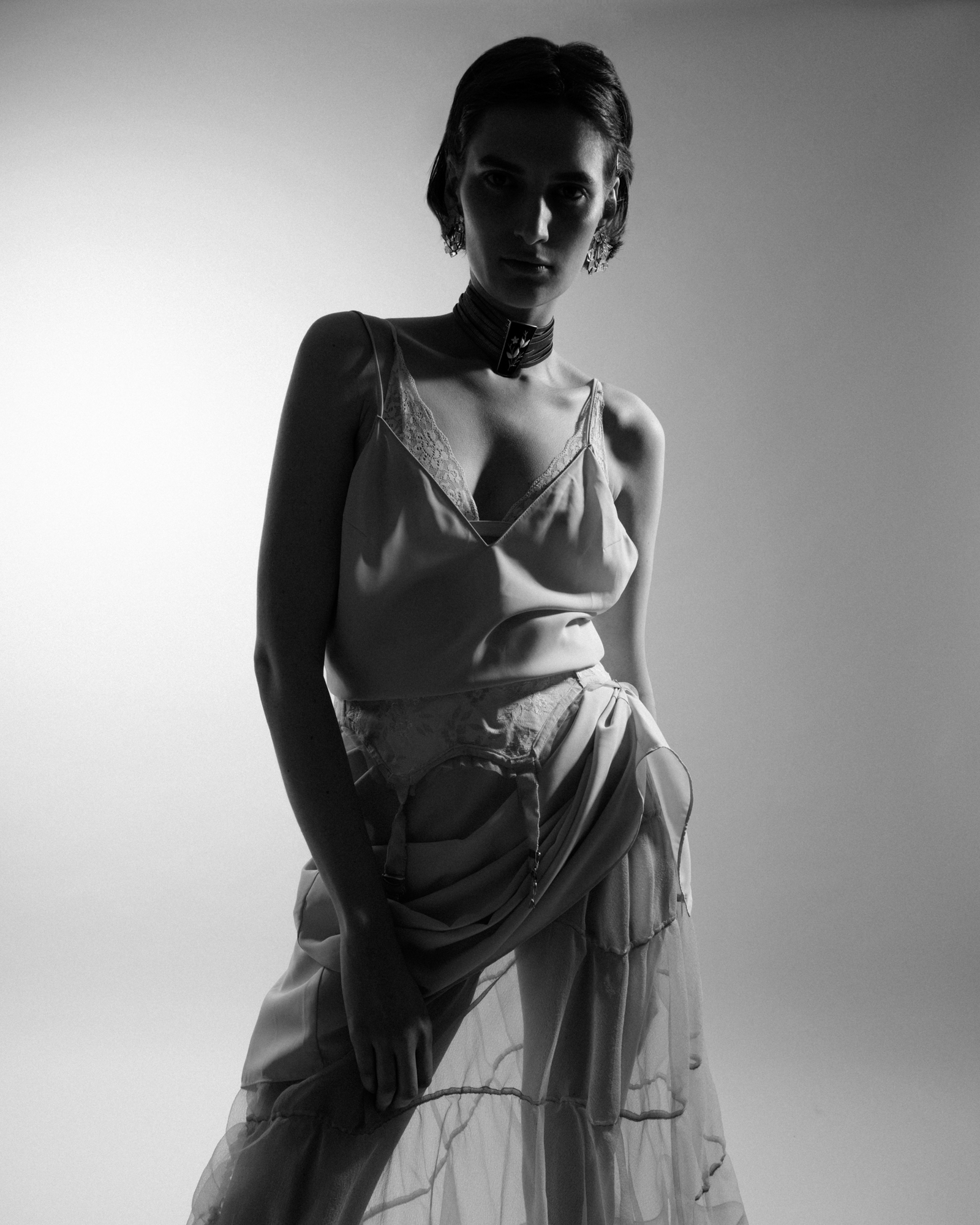 Black-and-white fashion portrait of a model wearing layered sheer clothing and a statement choker.
