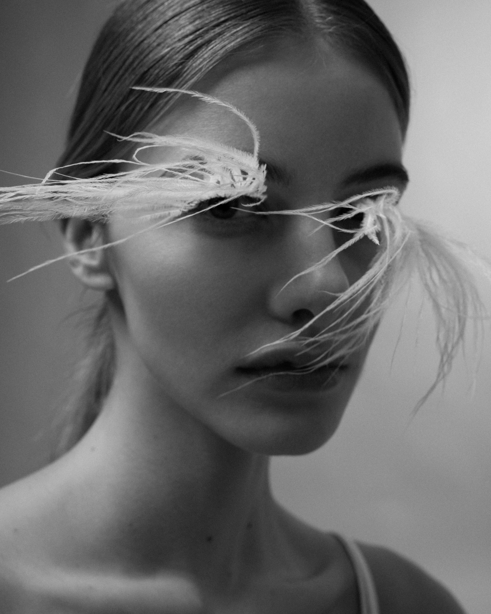 Black-and-white close-up beauty portrait of a woman with slicked-back hair and clear abstract material across her eyes.