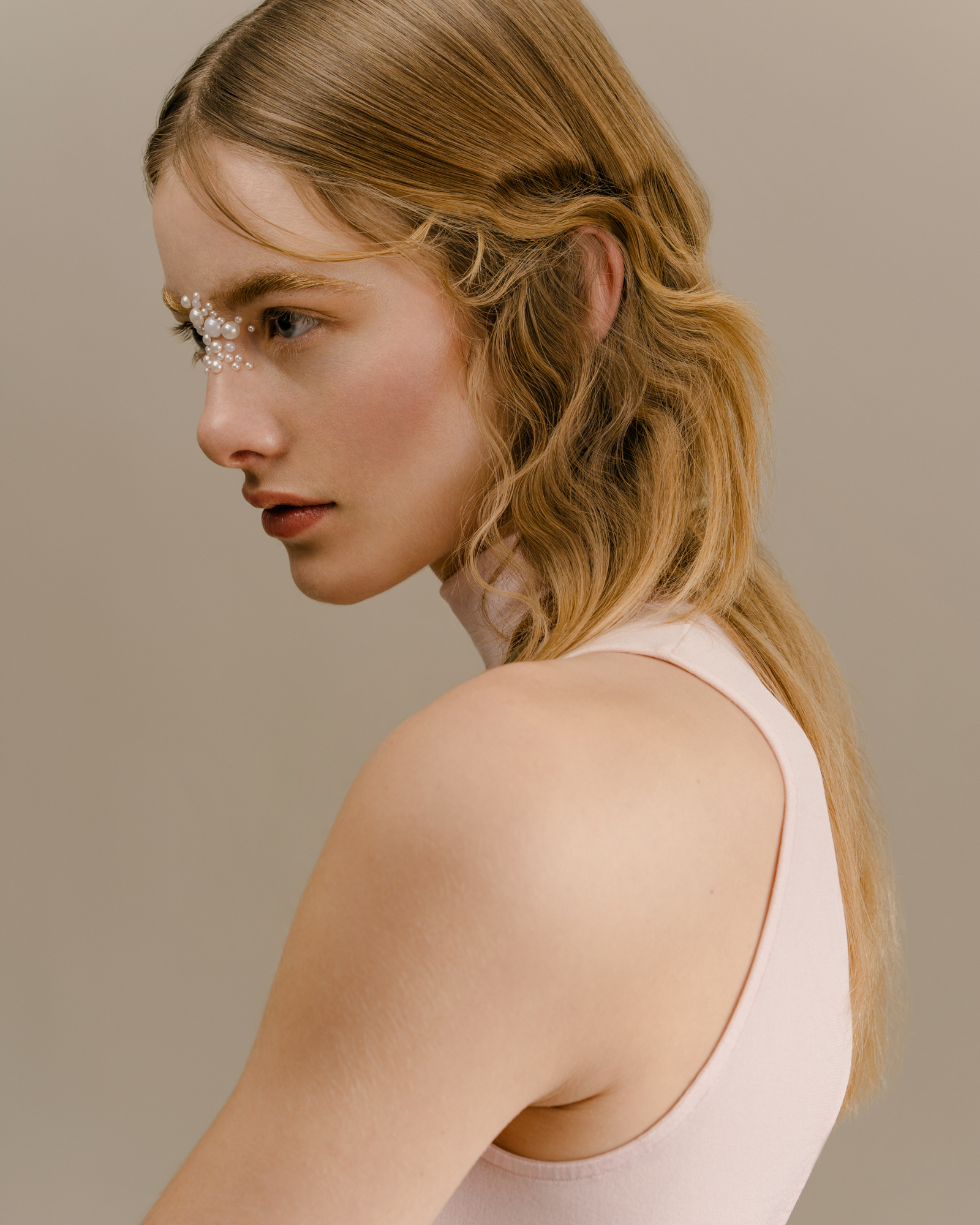 Portrait of a woman with damp wavy hair looking over her shoulder, wearing a white tank top against a neutral background.