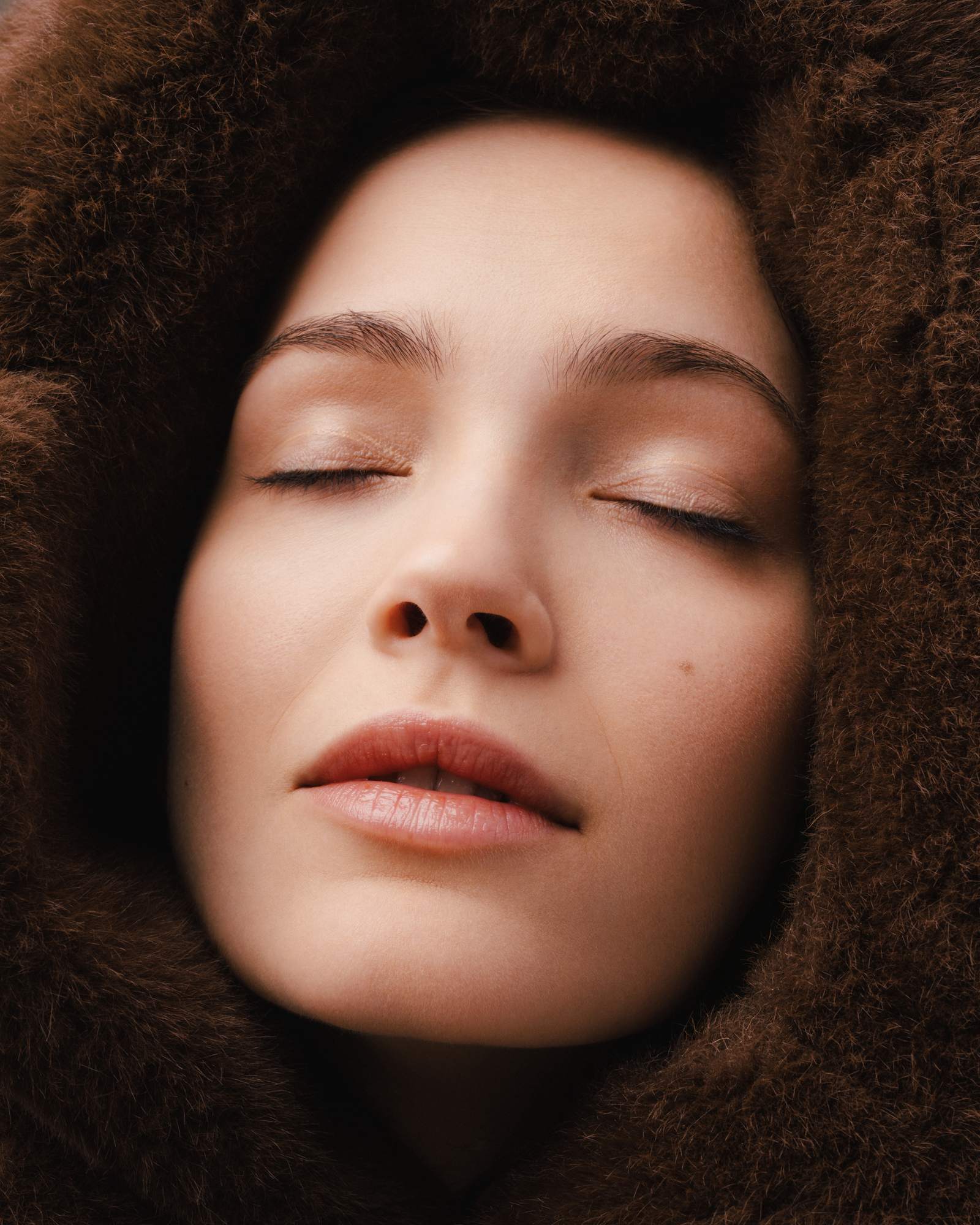 Close-up beauty portrait of a woman with curly hair and closed eyes, surrounded by a dark textured background