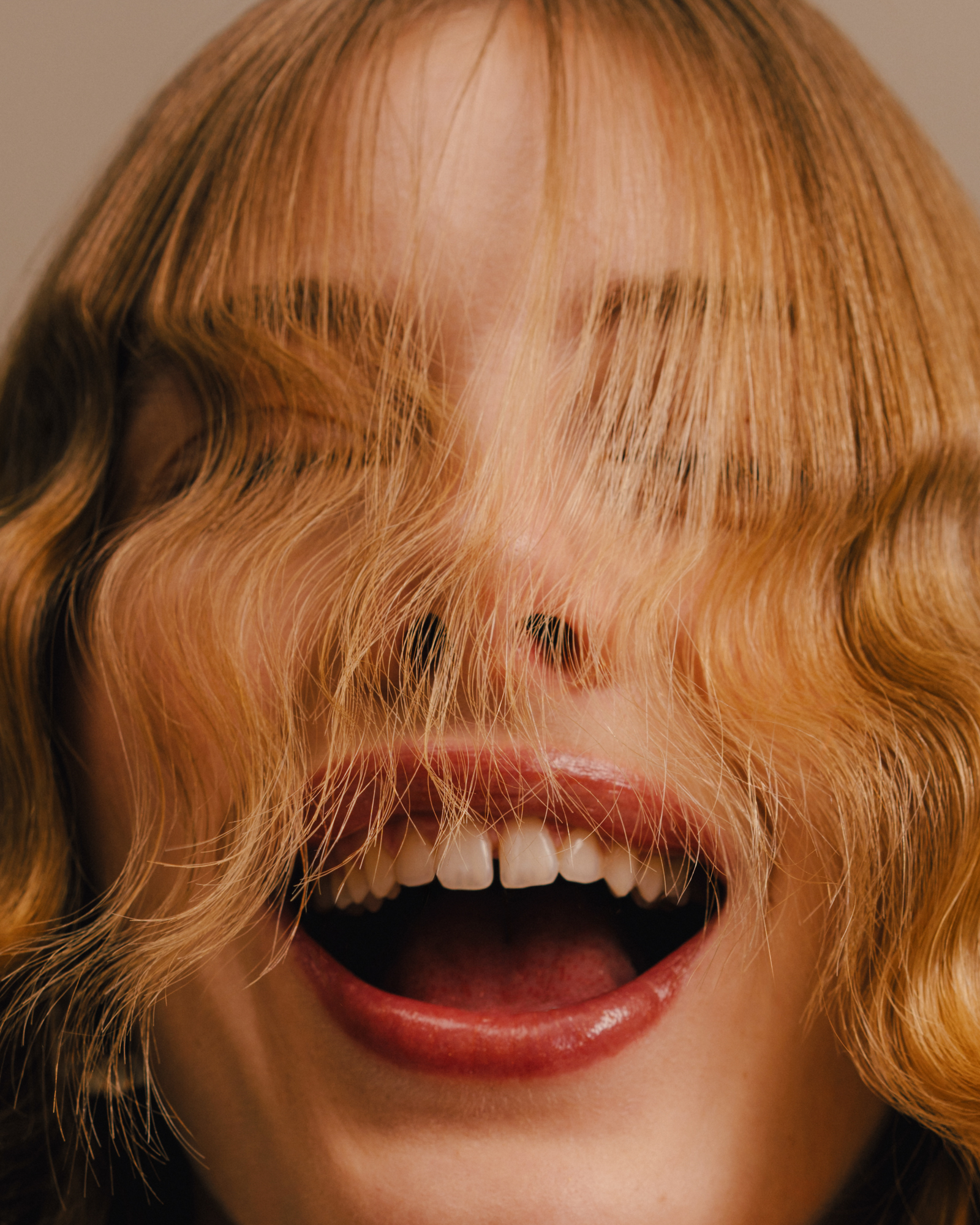 Close-up beauty portrait of a person smiling with blonde hair falling over their eyes and face.